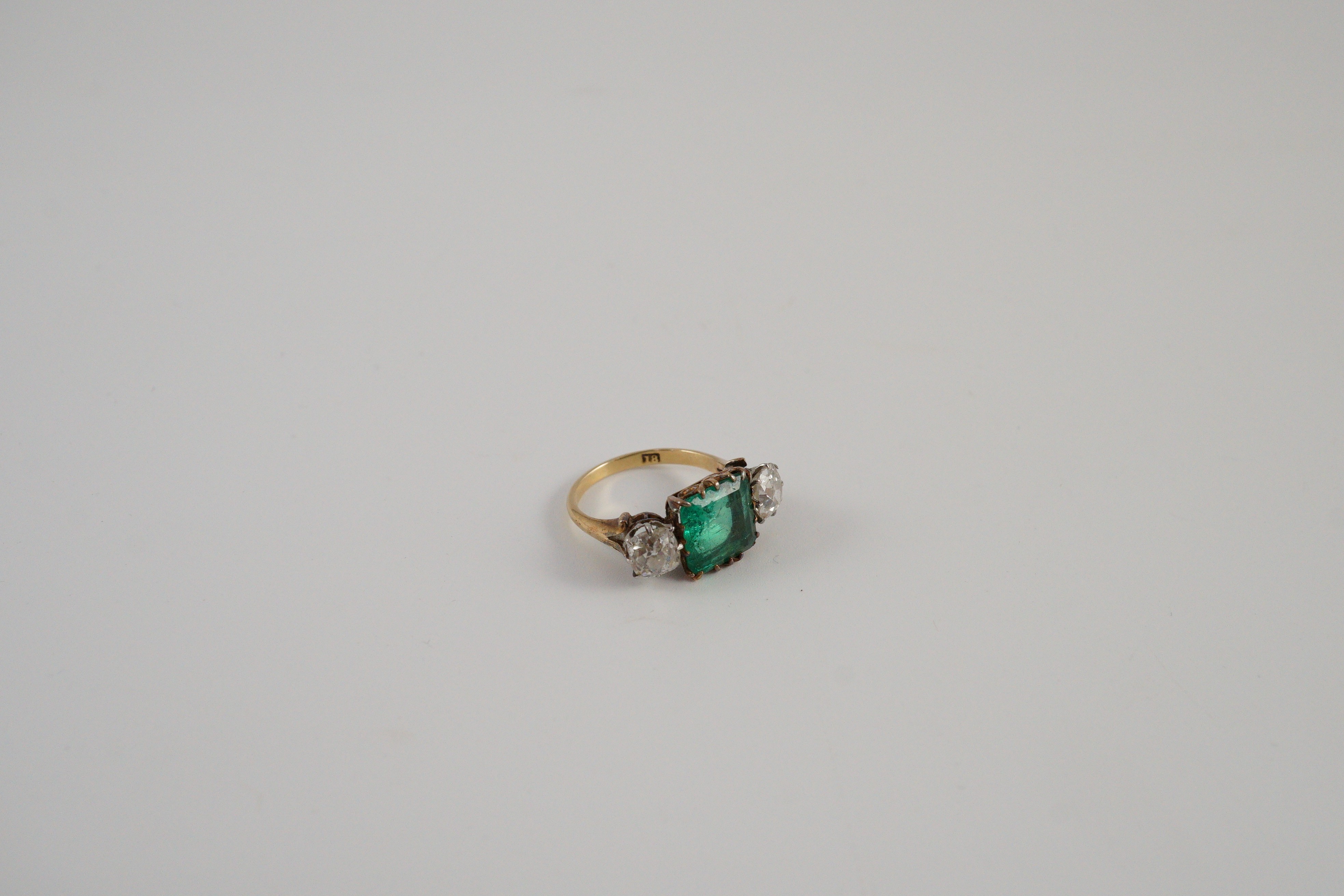 An early 20th century 18ct gold, square cut single stone emerald and two stone cushion cut diamond set dress ring